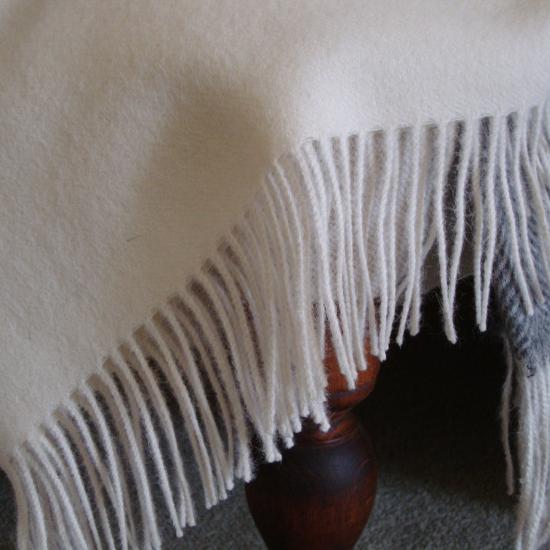 Luxuriously soft white alpaca throw with a delicate fringe, draped over a traditional wooden stool – part of our premium Alpaca Throws and Blanket Collection.