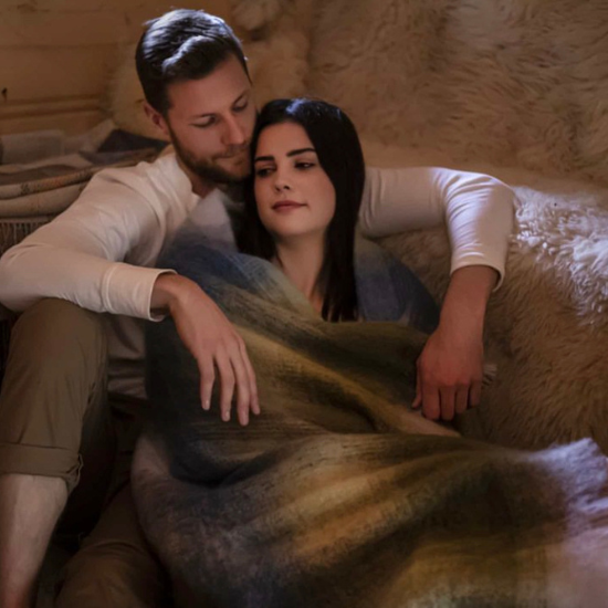 Couple cuddled together under a luxurious mohair throw in a softly lit room, capturing a romantic and heartfelt moment – a perfect anniversary gift idea from Solway Blankets.