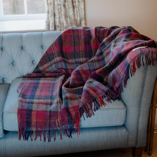 Rich red and navy tartan wool blanket draped over a light blue tufted sofa – adding warmth, texture, and classic British charm to a cosy living space.
