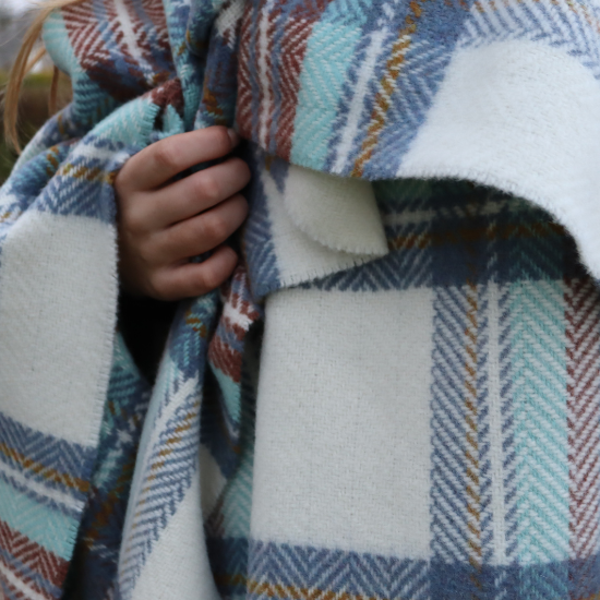 Close-up of a hand wrapped in a luxuriously soft cashmere blend blanket in soft blue, rust and cream check – the ultimate in warmth and refined comfort.