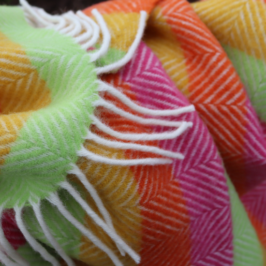 Bright and colourful herringbone wool blanket with playful stripes in pink, orange, yellow, and green—perfect for children's bedrooms or cosy storytimes.