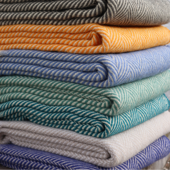 Stack of colourful eco-friendly and recycled wool blankets in chevron and herringbone weaves – part of the Eco-Friendly and Recycled Blanket Collection.