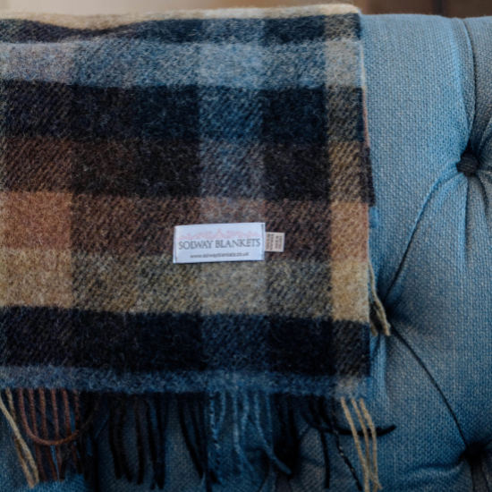 Earth-toned check wool blanket from Solway Blankets draped over a blue armchair – a timeless and thoughtful Father’s Day gift made in Britain.