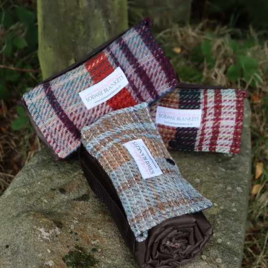 Compact, roll-up wool picnic blankets with waterproof backing, displayed on a stone - thoughtful and practical gifts under £50.