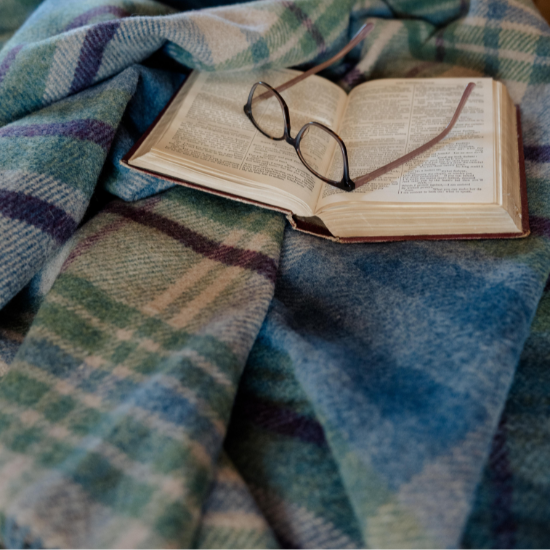 Soft blue and green wool blanket with an open book and reading glasses – a thoughtful and comforting gift idea for grandparents who cherish quiet moments.