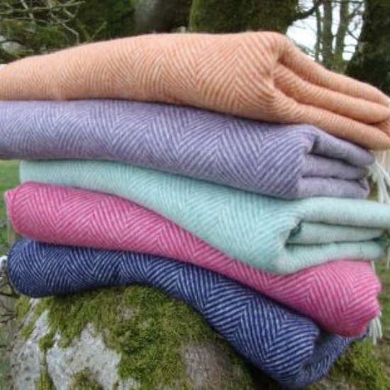 A colourful stack of wool throws in classic herringbone and fishbone weaves, featuring soft shades of orange, lilac, mint, pink, and navy—part of the Herringbone and Fishbone Blankets Collection.