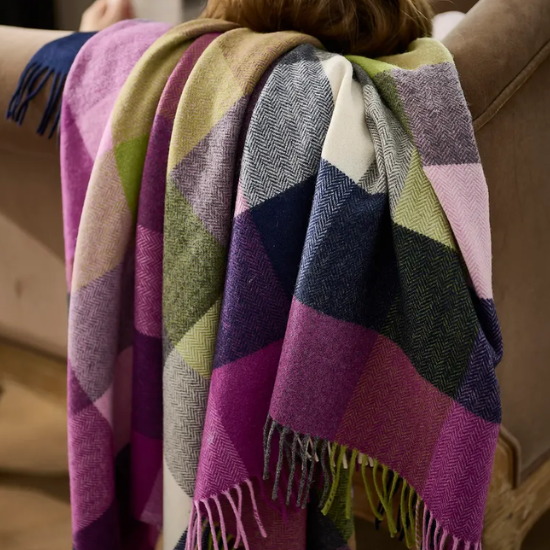 Luxuriously soft lambswool and merino throw in vibrant purples, greens, and blues draped over a sofa – part of the Lambswool and Merino Blanket Collection.