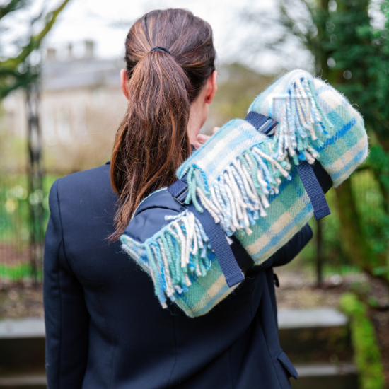 Woman carrying a rolled luxury wool picnic blanket with waterproof backing and leather-look straps – perfect for stylish outdoor dining and countryside escapes.