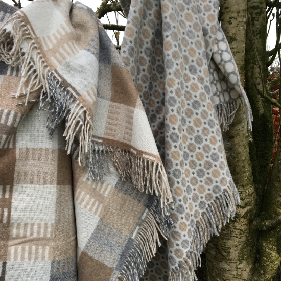 Two wool throws in warm neutral tones of cream, beige, and brown with soft patterns and fringe edges, hanging over a tree branch – part of the Solway Blankets Cream, Beige & Brown Collection.