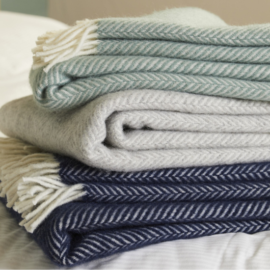Stack of herringbone-patterned throws in soft green, silver grey, and navy – from the Pure New Wool Blanket and Throw Collection.
