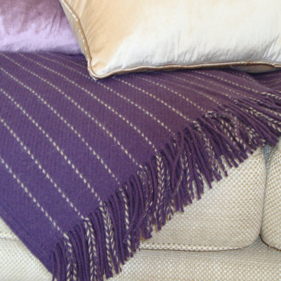 Luxurious deep purple wool throw with fine stripe detail and fringe, draped over a neutral sofa and styled with velvet and satin lilac-toned cushions – part of the Solway Blankets Purple and Lilac Collection.