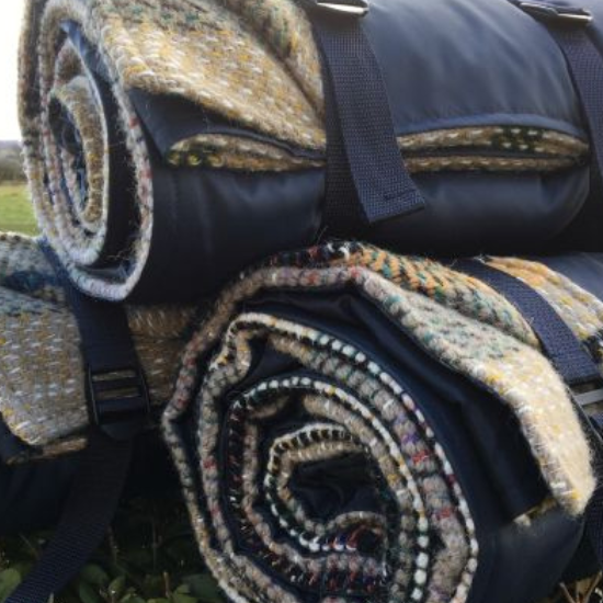 Rolled recycled wool picnic rugs with waterproof backing and carry straps, perfect for outdoor adventures and sustainable living.