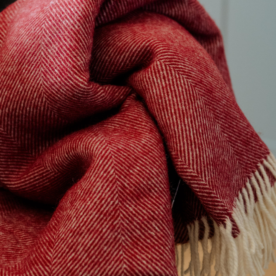 Close-up of a rich red herringbone wool blanket with soft cream fringe – showcasing luxurious texture, warmth and timeless British design.