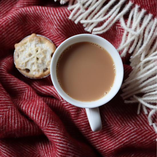 Cosy red herringbone wool throw with cream fringe, styled with a festive mince pie and a steaming cup of tea – perfect for thoughtful seasonal gifting from Solway Blankets.