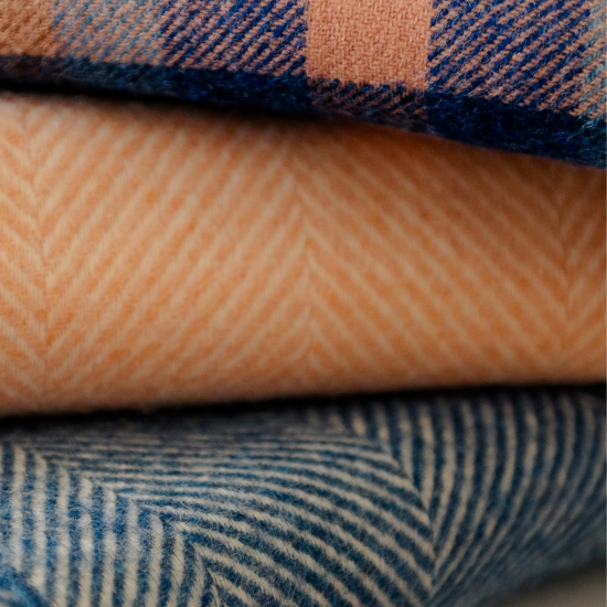 Stack of traditional Shetland wool blankets in soft peach, classic blue herringbone, and bold navy check—part of the Shetland Wool Blankets and Throws Collection.