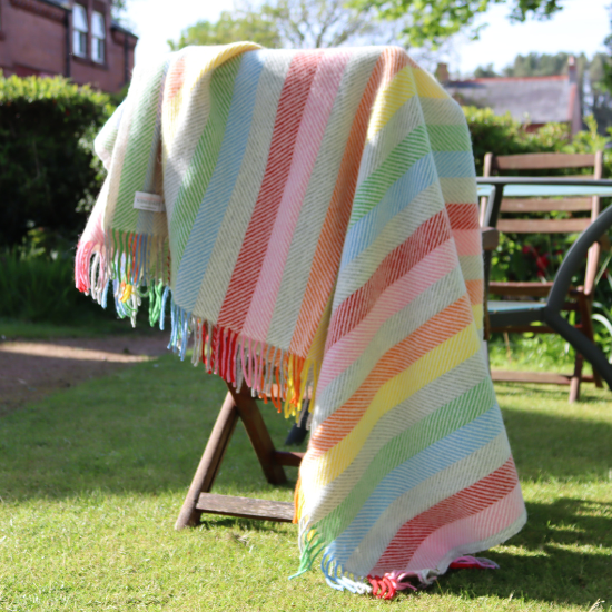 Colourful striped wool blanket draped over a garden chair in summer sunshine—perfect for outdoor living, picnics, and relaxing alfresco moments.