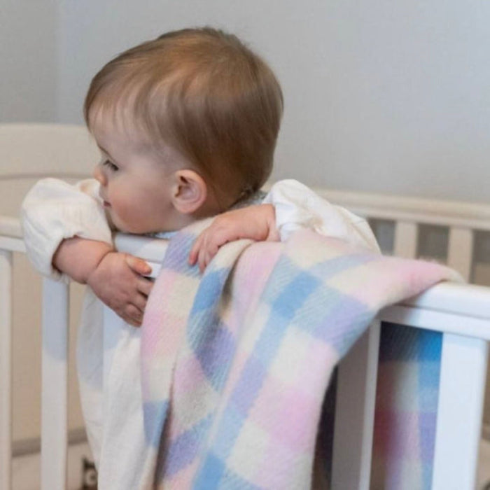 Child, baby holding a Limerick Pure New Wool Baby Blanket a check pink and blue in a crib cot