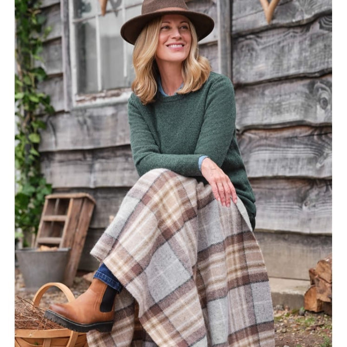 Person sitting outdoors with a neutral coloured plaid woolen blanket, wearing a green sweater and brown hat.