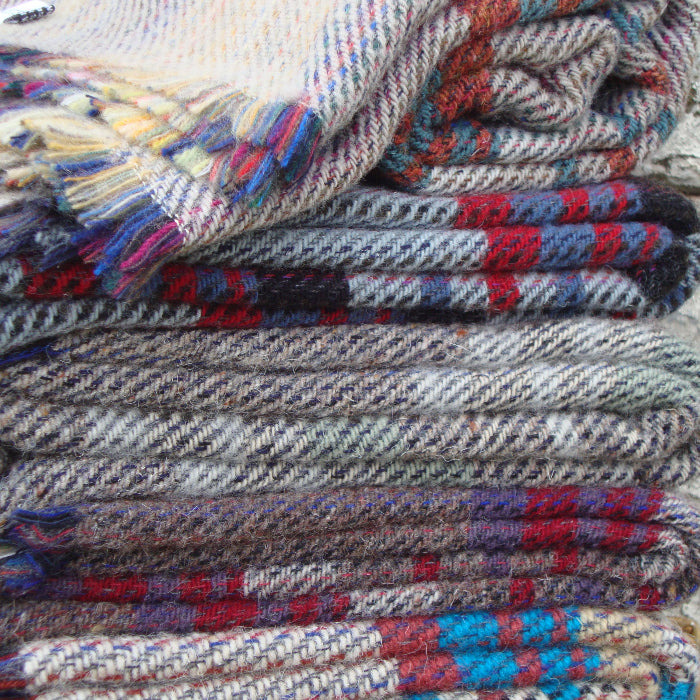 Stack of folded colourful patterned recycled blankets infront of a stone wall