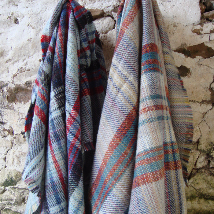 Differently coloured recycled plaid blankets hanging up on a stone wall