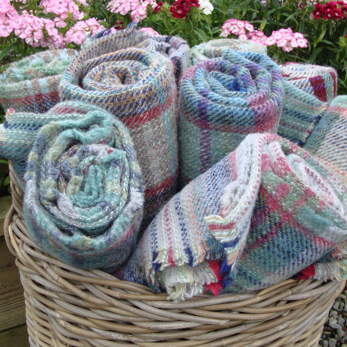 Basket of multiple rolled up colourful knitted blankets with flowers in the background