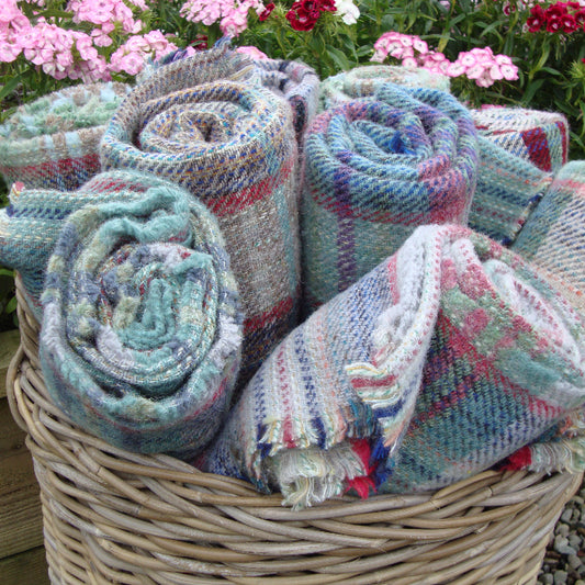 Basket of multiple rolled up colourful knitted blankets with flowers in the background