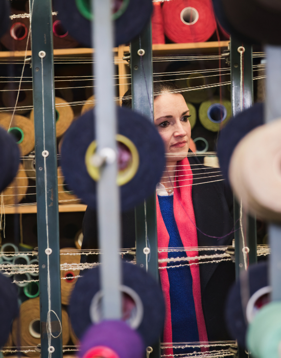 Victoria Lane owner and founder standing behind a loom with colourful yarn spools in a blanket weaving mill
