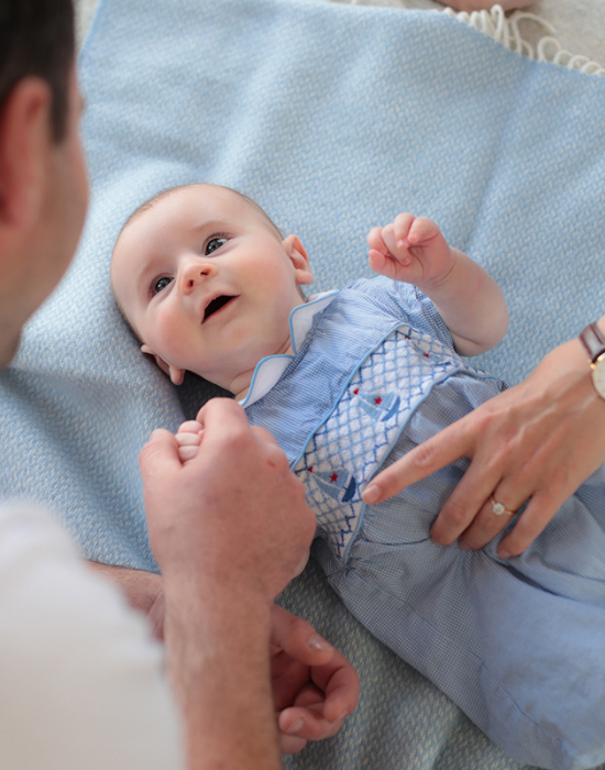 Baby lying on a Solway Blankets blue cashmere baby blanket with parents interacting 