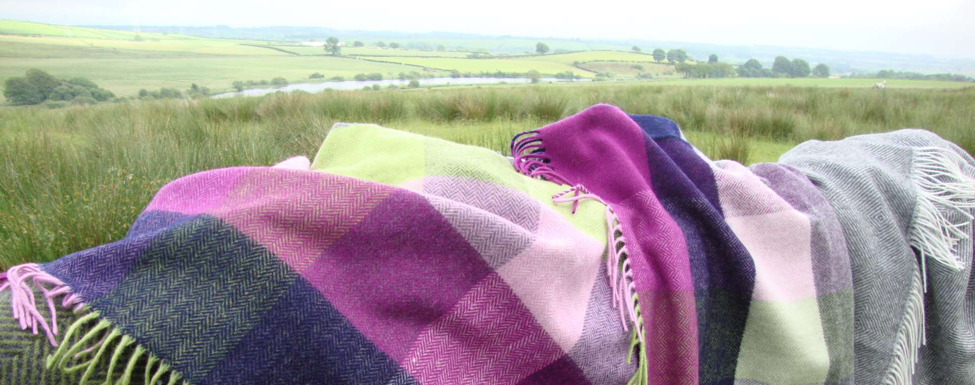 Vibrant check blanket draped over a a fence with a beautiful scenic Scottish background, hills and loch.