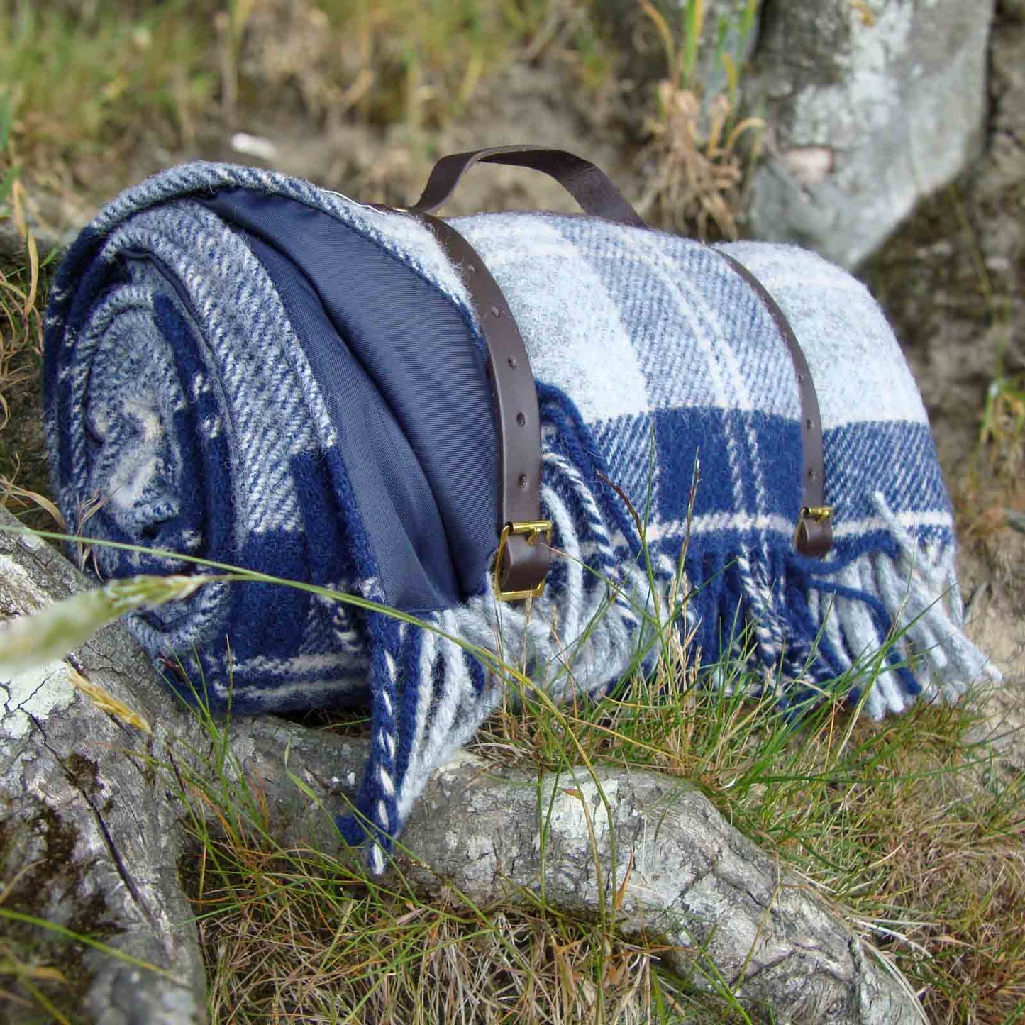 Blue and white Banockbane tartan checkered picnic blanket with leather straps on a tree branch in a natural 