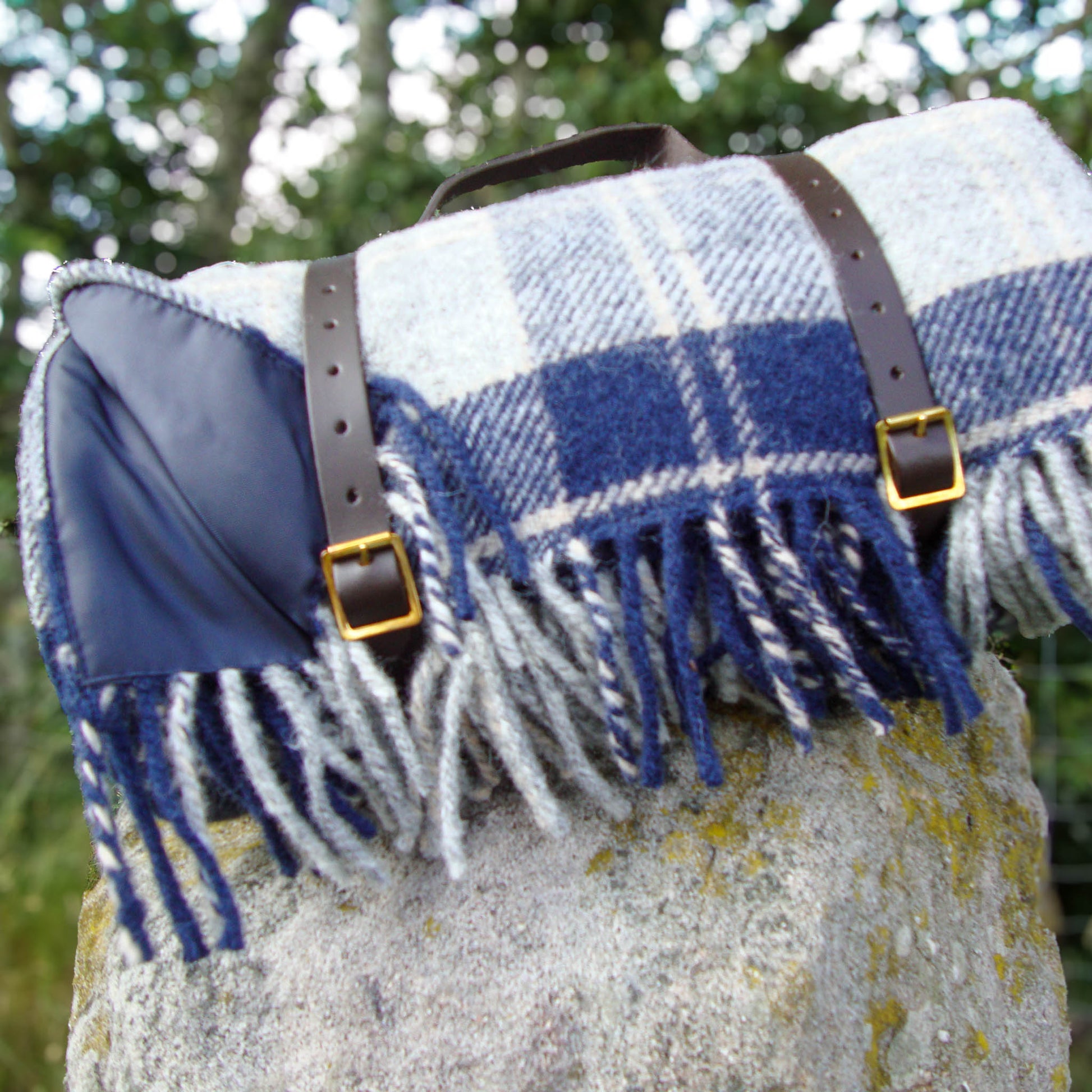 Blue and white Bannockbane tartan plaid picnic blanket with waterproof back and leather straps on a stone gatepost outdoors