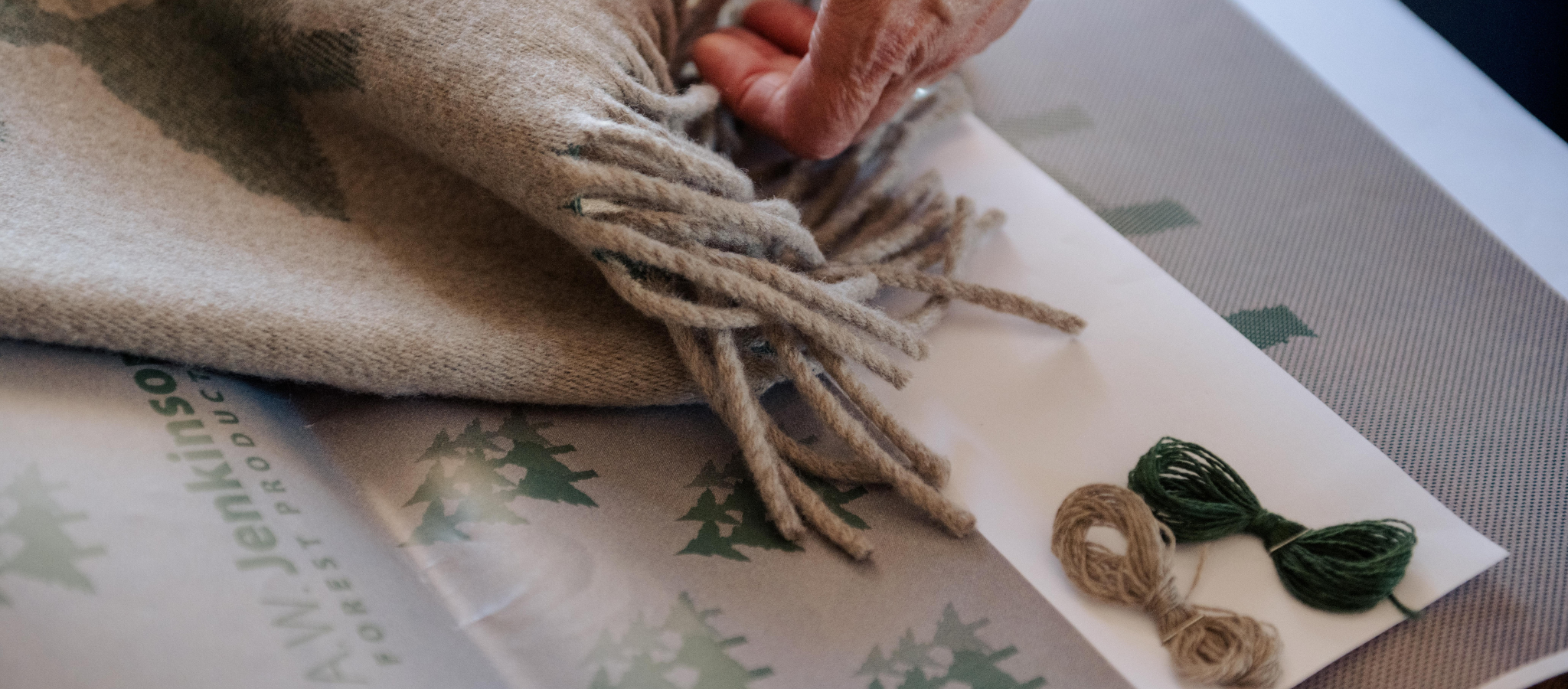 Person holding a custom designed blanket with company logo woven in and tassels on a surface with design artwork and coloured yarn samples