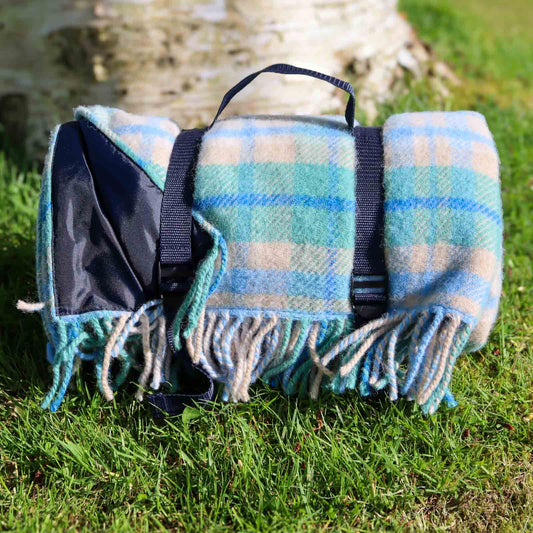 blue cottage check waterproof picnic blanket with navy carry straps on grass