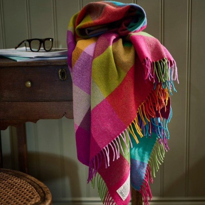 Colorful vibrant plaid throw draped over a wooden chair with a wooden table in the background.