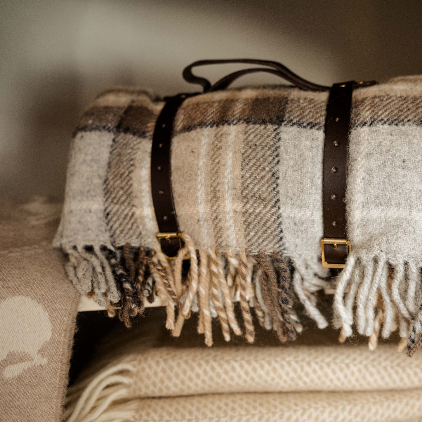 McKellar Tartan Luxury Picnic blanket with waterproof backing, fringe and leather straps styled on a shelf