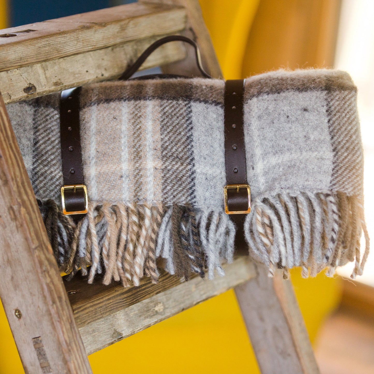 McKellar Tartan Luxury pure wool waterproof picnic blanket with leather straps on a wooden ladder against a blurred background