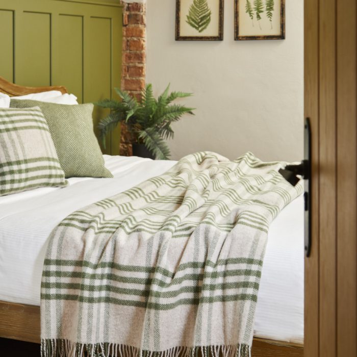 Nature themed interior styling of a bedroom with a bed covered with the Hex extra large Solway Blanket in green and white plaid check, green cushions, plants and framed pictures on the wall.