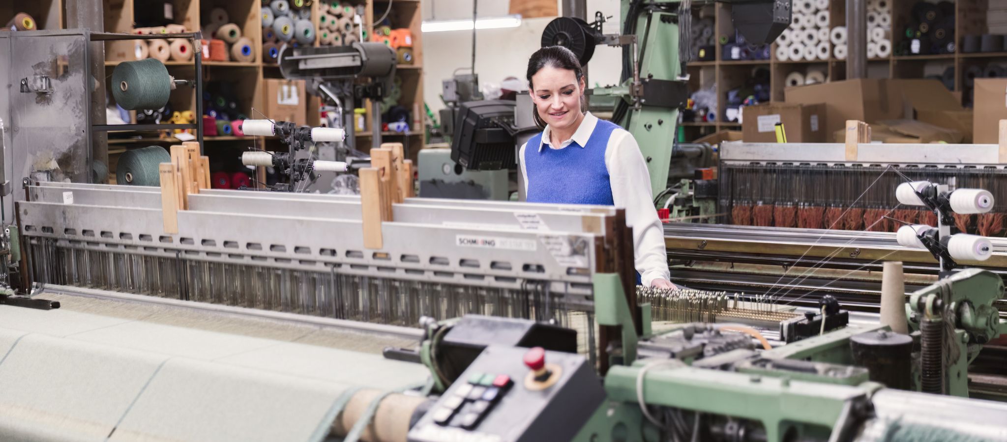 Victoria Lane of Solway Blankets in traditional Scottish textile weaving mill, viewing the loom set up with yarn cones in the background