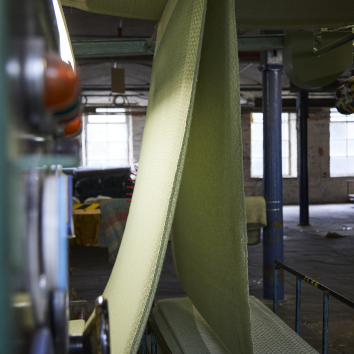 A length of green woven blanket cloth being raised in a traditional mill, prior to cutting and finishing.