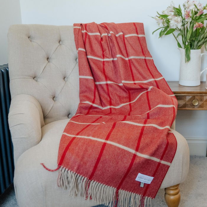 A red and off white/grey check cashmere wool throw blanket with fringe is draped over a beige tufted armchair in a living room setting.