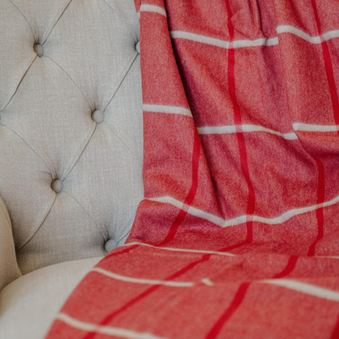 A close-up of a red and pale grey check pure cashmere blanket draped over a light beige tufted armchair.