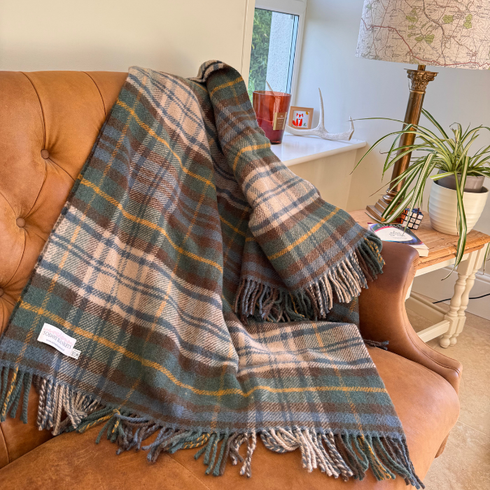 A large Antique Dress Gordon tartan fringed throw blanket draped over a tan leather armchair in a cosy living room setting.