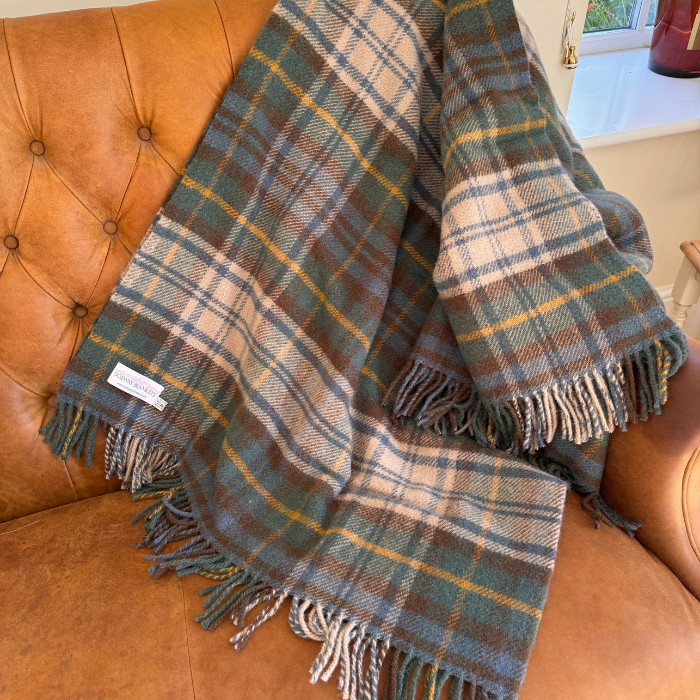 A close-up of the Antique Dress Gordon plaid wool blanket with fringe, featuring muted toned green, blue, brown, off white and yellow checks. A white woven label reading 'SOLWAY BLANKETS' 