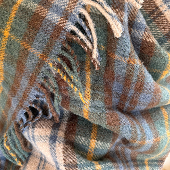 A close-up of a Antique dress Gordon blanket with fringe, featuring muted green, brown, blue and yellow, draped to show texture and fringe detail