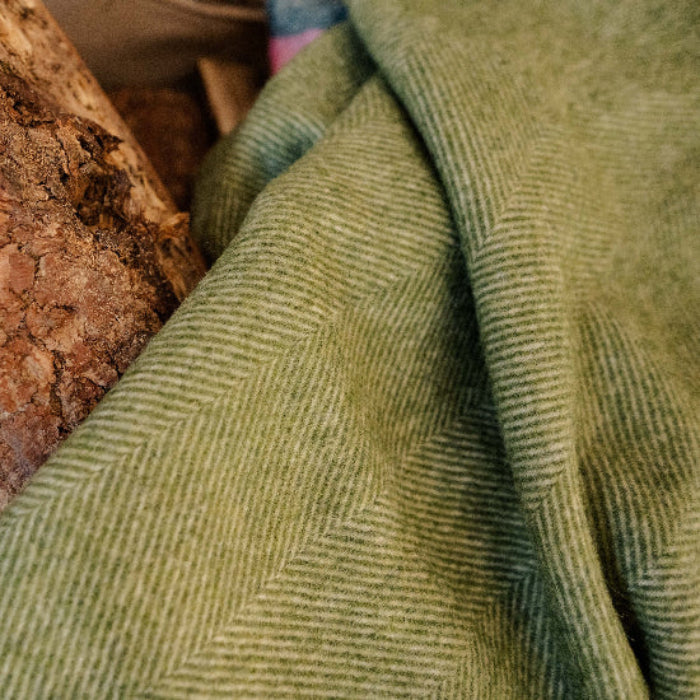 Close-up of Apple Green Wool Blanket with a herringbone pattern against a wooden background