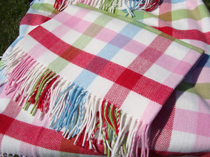 A close-up of the bold Baby Bunting Cashmere Mix check blanket with multicoloured fringe, featuring a check pattern of pink, red, light blue, and green checks on a white base.