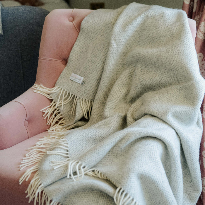 Grey silver wool blanket draped over a pink chair with a floral curtain in the background