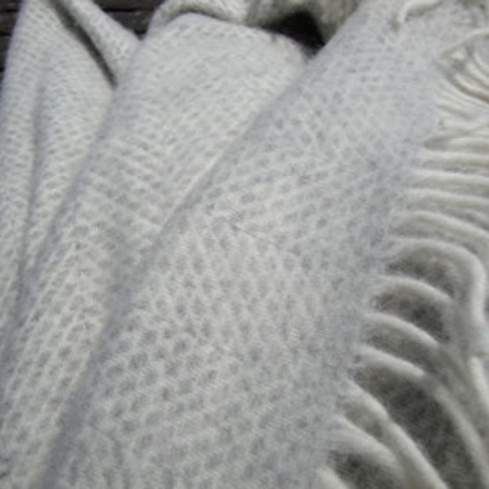 Grey silver textured woolen blanket with white fringe on a dark background
