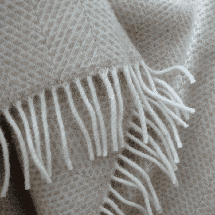 Detailed close-up of beige blanket with white fringes, highlighting beehive weave texture