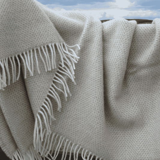 Beige blanket with beehive pattern and white fringes, draped over a chair with a sky backdrop